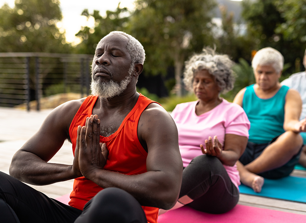 Senior multiracial friends meditating while sitting on mats agai